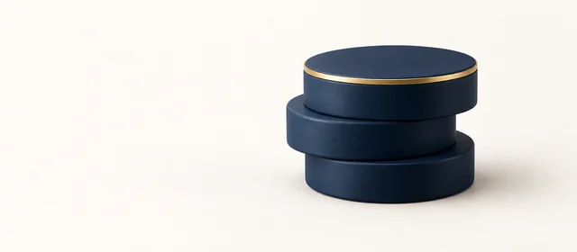 Three stacked matte navy discs with a gold rim on top, on warm paper.