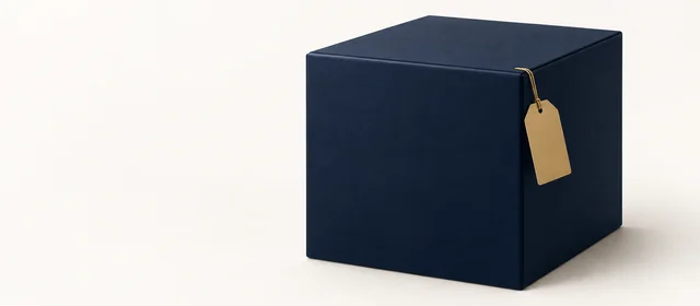 A matte navy parcel box with a small gold shipping tag, on warm paper.
