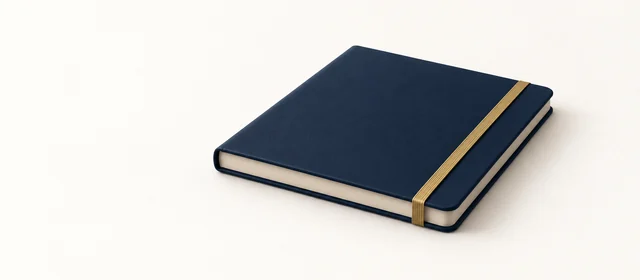 A closed matte navy notebook with a gold elastic band, on warm paper.