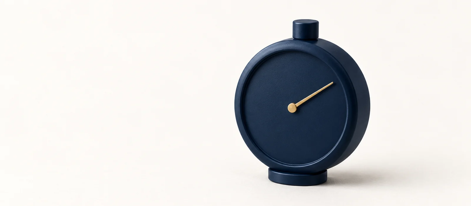 A matte navy stopwatch with a plain dial and a single gold needle, on warm paper.
